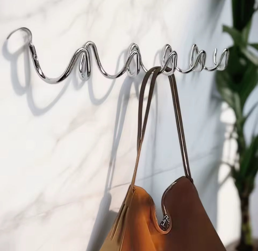Modern metal wall hook with a brown handbag hanging on it